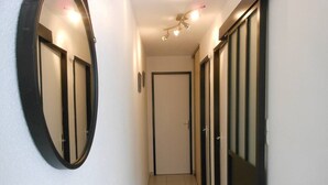 Un couloir étroit, avec un miroir sur le côté gauche, une porte au fond et un luminaire au plafond.
