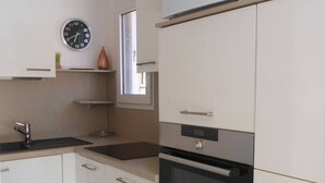 Une cuisine moderne avec des meubles blancs, un four noir, un évier en acier inoxydable et une horloge murale.