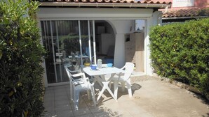 Un espace patio aménagé avec une table et des chaises, entouré de verdure et doté d’un sol carrelé.