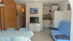 Un espace de vie compact comprenant un coin repas, une kitchenette et un canapé bleu.