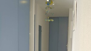 Un couloir étroit, avec une porte bleue au fond, un ventilateur de plafond orné d’un motif de poisson et un sol carrelé.