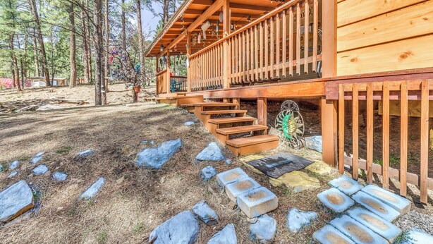 Una cabaña de madera con un porche y escalones que llevan a una terraza, rodeada de árboles y rocas.