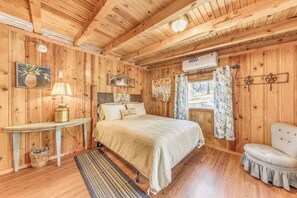A wooden cabin bedroom with a bed, a small table, a chair, and a window with curtains. - Ruidoso Cabin w/ Hot Tub - 2 Mi to Grindstone Lake (Ruidoso)
