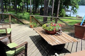 A wooden deck with wicker chairs and a table, surrounded by potted plants and overlooking a lake.