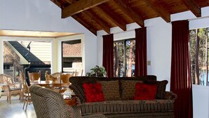 Un salón amplio con techo de madera, un sofá con cojines rojos y una zona de comedor con sillas y una mesa.