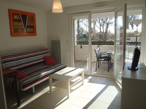 A modern living room with a striped sofa, a white coffee table, and a glass door leading to a balcony with a table and chairs.