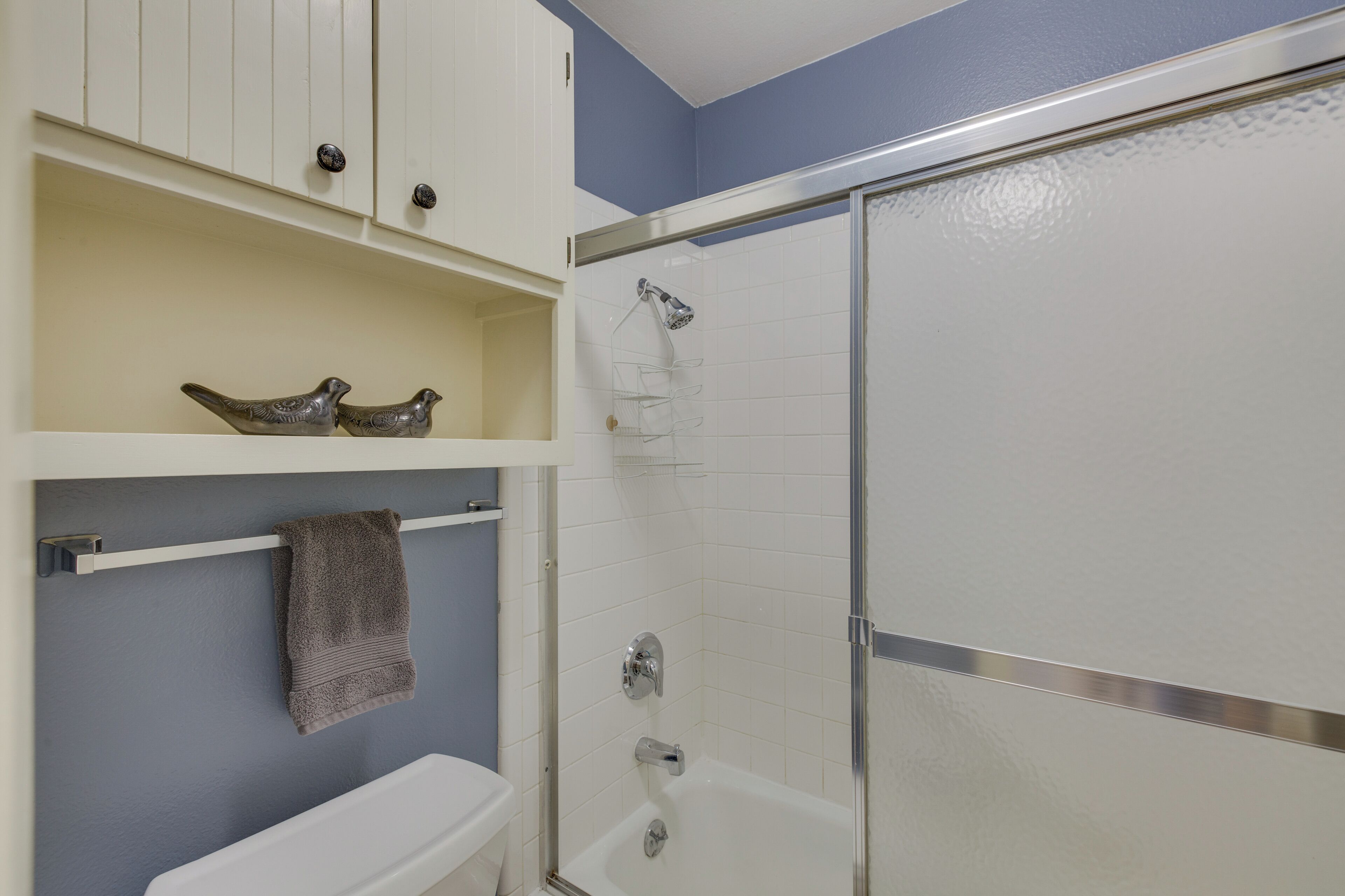 Une salle de bain avec des toilettes blanches, un espace douche et une étagère ornée d’objets décoratifs.