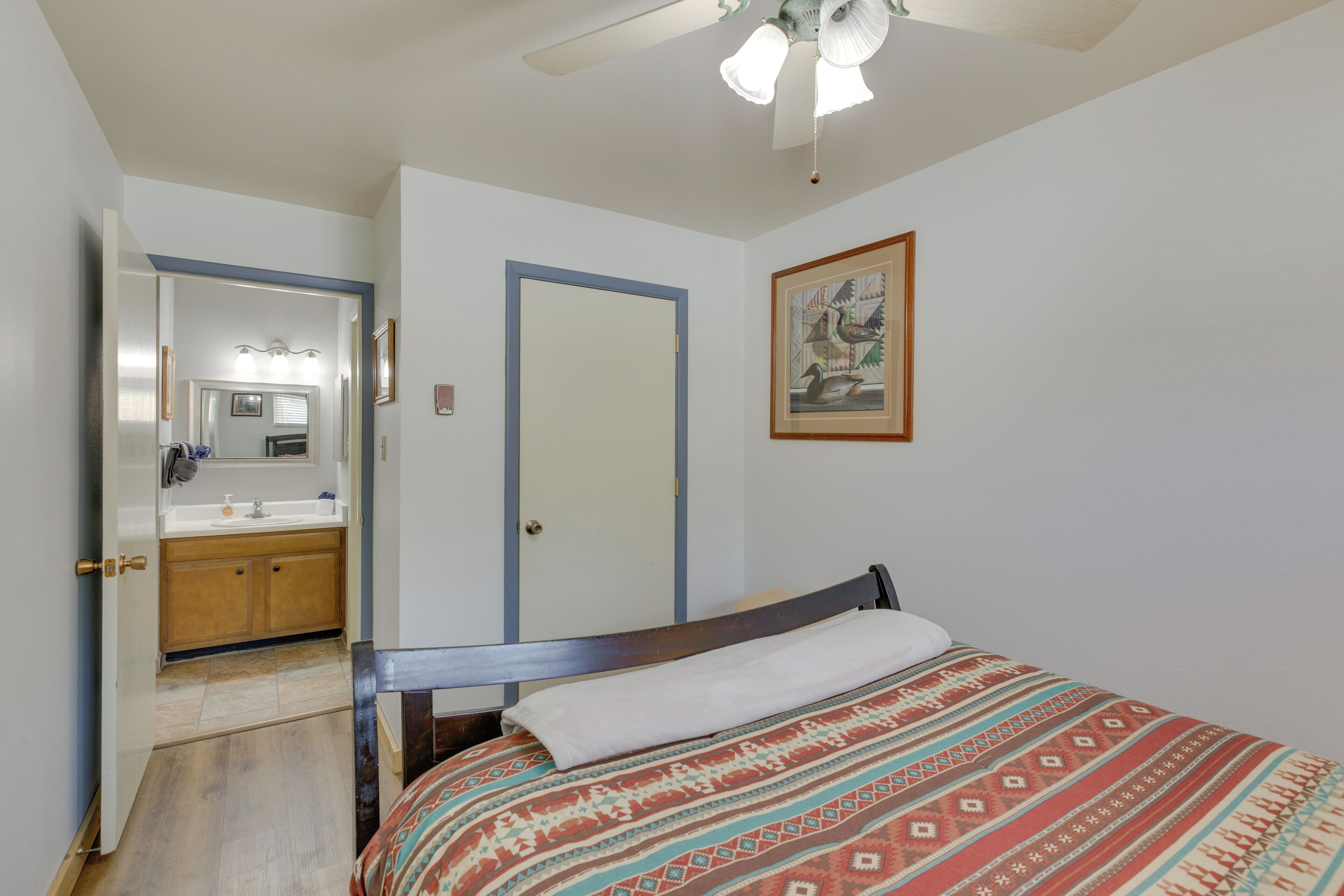 Une chambre à coucher comprenant un lit, une table de chevet, un miroir, une porte et une salle de bain avec un lavabo et un miroir.
