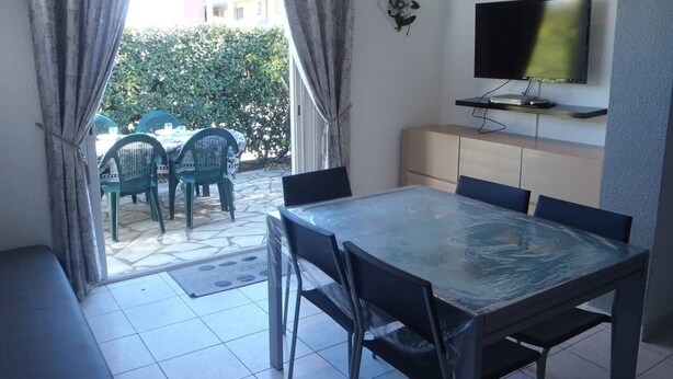 A dining area with a glass table and chairs, a TV mounted on the wall, and a view of the outside through a glass door. - VILLA  3 ROOMS MEZ 41m2 + TERRACE 12m2 REF 4027 (MARSEILLAN PLAGE)