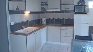 A compact kitchen with a sink, cabinets, a microwave, and a clock. - VILLA  3 ROOMS MEZ 41m2 + TERRACE 12m2 REF 4027 (MARSEILLAN PLAGE)