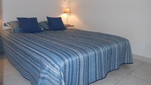 A bedroom with a large bed, two pillows, a nightstand, and a wall-mounted lamp. - VILLA  3 ROOMS MEZ 41m2 + TERRACE 12m2 REF 4027 (MARSEILLAN PLAGE)
