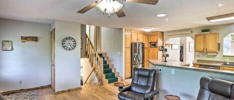 A spacious living room with a ceiling fan, a fireplace, and a view of the kitchen and staircase.