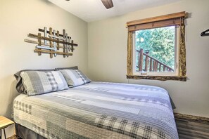 Un dormitorio con cama, cabecera de madera, ventana con vista a una terraza de madera y una obra de arte de madera colgada en la pared.