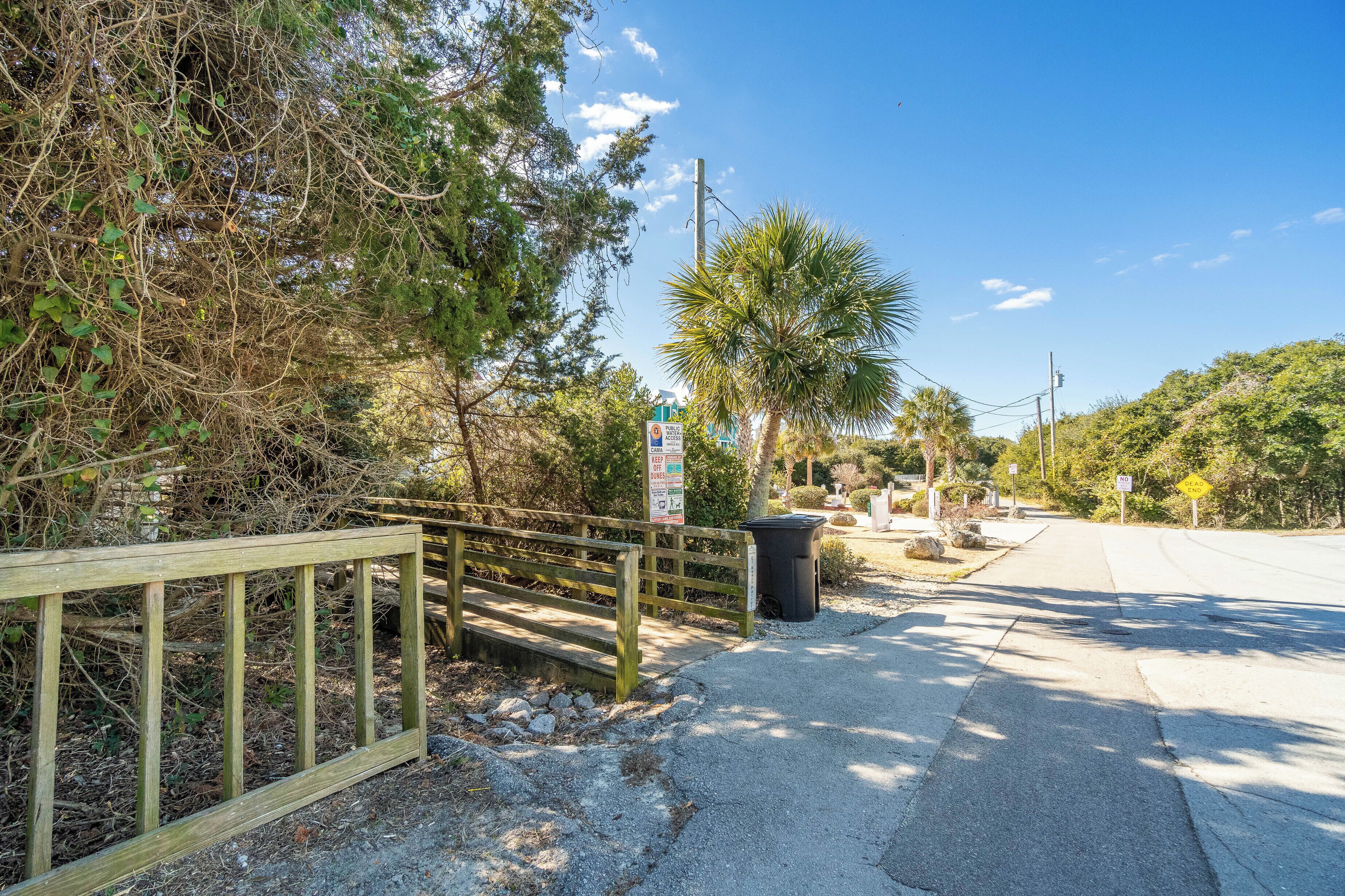 A paved pathway with a wooden fence on the left, surrounded by trees and vegetation.