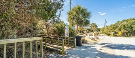 A paved pathway with a wooden fence on the left, surrounded by trees and vegetation.