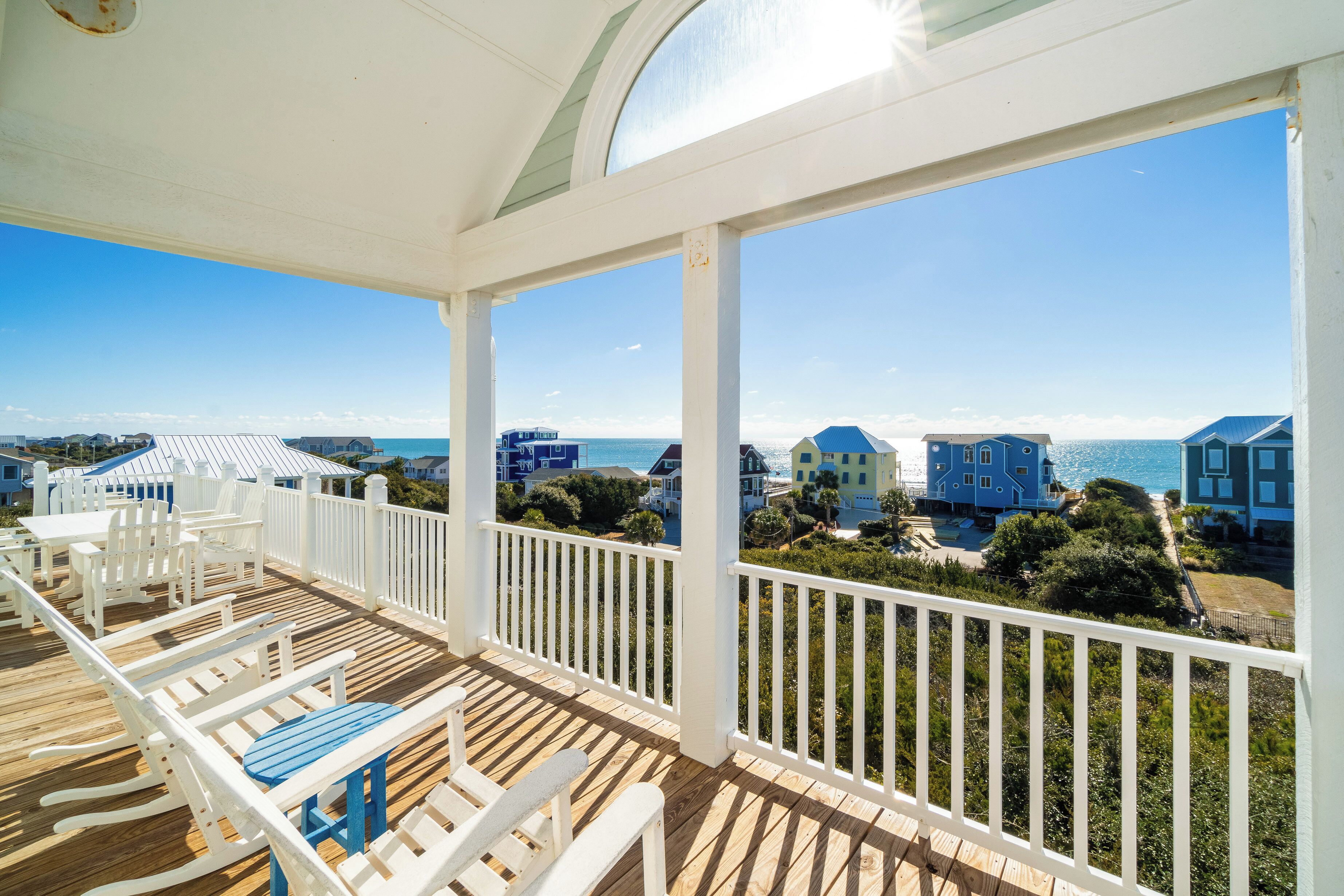 A covered outdoor deck with white railings, wooden flooring, and blue and white furniture.