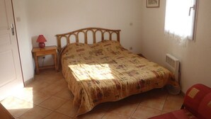 Une chambre à coucher comprenant un lit, une table de chevet, une chaise, un radiateur et une fenêtre avec des rideaux.