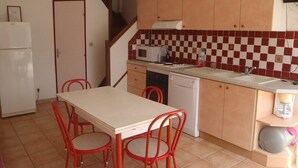 Une cuisine compacte comprenant une table et des chaises, un four à micro-ondes, un lave-vaisselle et un pare-feu à carreaux.