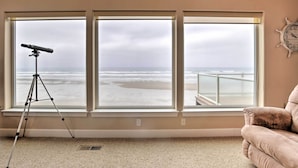 A room with large windows overlooking the ocean, a telescope on a tripod, and a clock on the wall. - Oceanfront South Beach Home w/ Hot Tub & Sauna (South Beach)