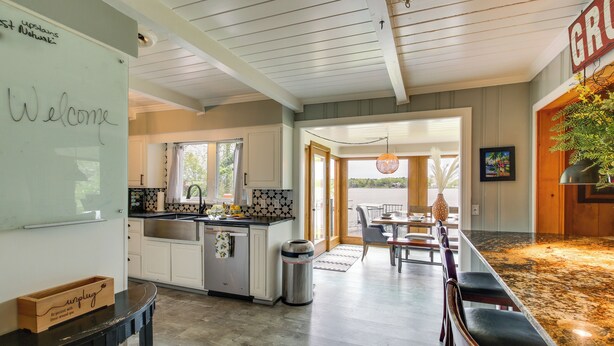 A modern kitchen with white cabinets, a black countertop, and a whiteboard with 'Welcome' written on it. - Decks & Lake Views: Waterfront Hot Springs Home! (Hot Springs)