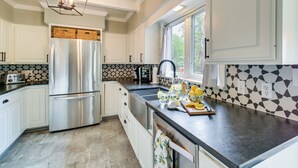 A modern kitchen with white cabinets, a stainless steel refrigerator, a black countertop, and a window with blinds. - Decks & Lake Views: Waterfront Hot Springs Home! (Hot Springs)