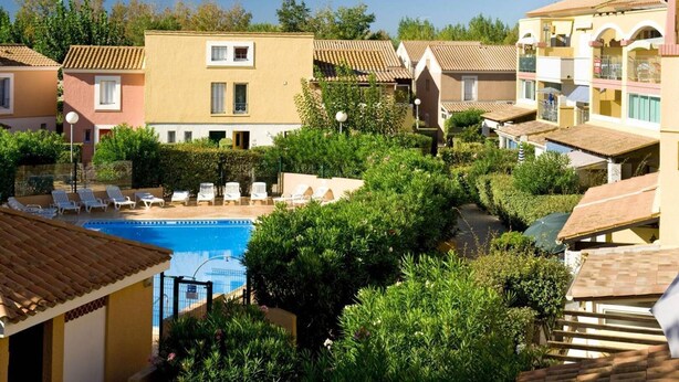 A residential area with a swimming pool surrounded by greenery and multiple buildings with tiled roofs. - APT 3 ROOMS 36m2 + LOGGIA  7m2 REF 4031 (MARSEILLAN PLAGE)