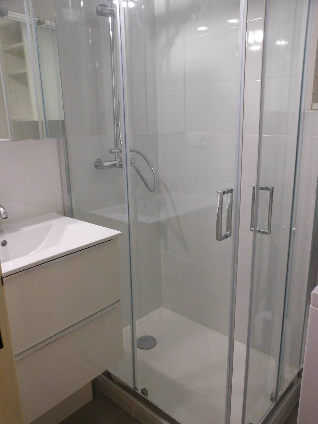 Une salle de bain moderne avec une douche à parois de verre, un lavabo blanc et un miroir.