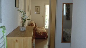 A narrow hallway leading to a bedroom with a bed and a window. A wooden counter with a vase of flowers is visible on the left. - APT 3 ROOMS 36m2 + LOGGIA  7m2 REF 4031 (MARSEILLAN PLAGE)