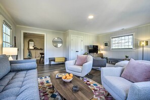 A modern living room with grey sofas, a coffee table with a bowl of fruit, and a TV in the background. - Charming Carrboro Home - Walk to Downtown! (Carrboro)