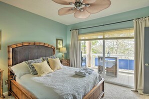 A bedroom with a large bed, a ceiling fan, a window with curtains, and a view of the outside.