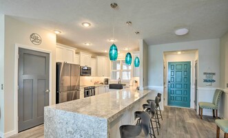 Una cocina moderna con armarios blancos, una isla grande, electrodomésticos de acero inoxidable y lámparas colgantes color turquesa.