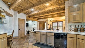 A spacious kitchen with wooden cabinets, a large island with a dishwasher, and a rustic ceiling. - Las Cruces Home 'La Casa Blanca' w/ Courtyard (Las Cruces)