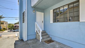 Un immeuble résidentiel avec un escalier en béton, une porte blanche et une fenêtre avec des volets.