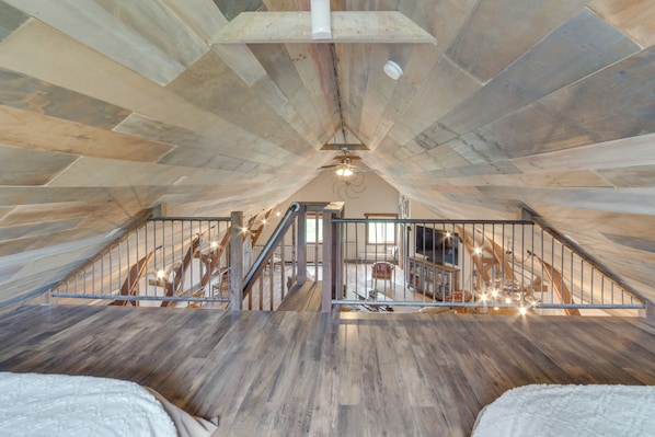 An attic bedroom with a sloped ceiling, wooden beams, a staircase, and a chandelier. - Unique, Renovated Barn Vacation Rental in Donnelly (Donnelly)