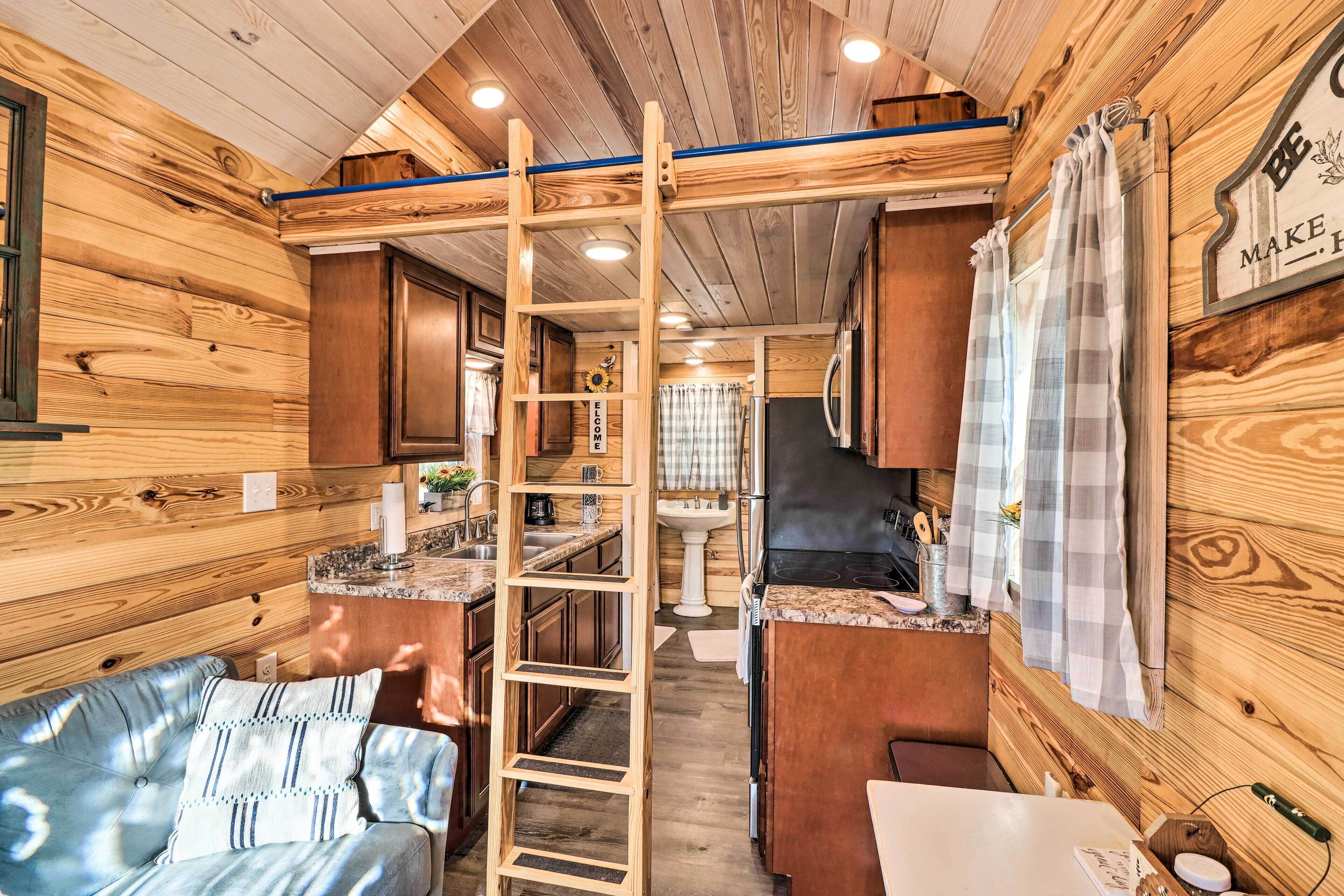 A cozy cabin interior with a wooden interior, a sofa, a ladder, a kitchenette, and a bathroom.
