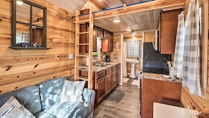 A cozy cabin interior with a wooden interior, a sofa, a kitchen area, and a bathroom. - La Petite Maison in Mount Olive w/ Fire Pit! (Mountain View)