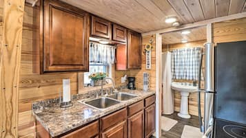 A kitchen with wooden cabinets, granite countertops, stainless steel sinks, a refrigerator, and a sink with a pedestal.