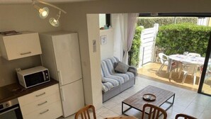A compact kitchen with a microwave, refrigerator, and oven, a dining table with chairs, and a view of a patio with a sofa and outdoor furniture. - VILLA  3 ROOMS MEZ 48m2 + TERRACE 7m2 REF 4034 (MARSEILLAN PLAGE)