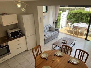 A compact kitchen with a microwave, refrigerator, and oven, a dining table with chairs, and a view of a patio with a sofa and outdoor furniture. - VILLA  3 ROOMS MEZ 48m2 + TERRACE 7m2 REF 4034 (MARSEILLAN PLAGE)