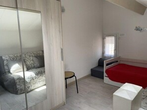 Um quarto com cama, sofá, uma mesinha e guarda-roupa.