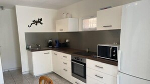 A compact kitchen with white cabinets, a microwave, a stove, and a sink. - VILLA  3 ROOMS MEZ 48m2 + TERRACE 7m2 REF 4034 (MARSEILLAN PLAGE)