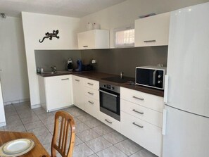 Pieni, käytännöllinen keittiö, jossa on valkoiset kaapit, mikroaaltouuni, liesi ja pesuallas.