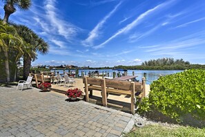 A waterfront patio with wooden benches, potted plants, and a view of the water. - Beachfront Englewood Condo w/ Community Pool! (Englewood)