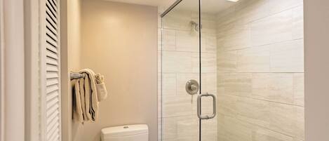 A modern bathroom with a glass shower enclosure, a toilet, and a towel rack.