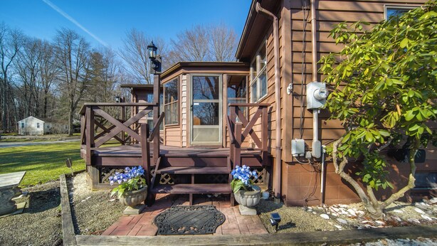 Ein Holzhaus mit einer Veranda, ein kleiner Garten mit Kübelpflanzen und einem blauen Himmel.