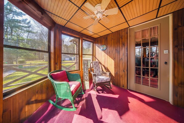 A wooden-paneled room with a rocking chair, a chair with a floral cushion, and a large window offering a view of a yard. - Charming Pymatuning Lake House Near Park & Beach (Andover)