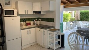 A compact kitchen with white cabinets, a microwave, a small refrigerator, and a dishwasher. There is a small island with a sink and a chair. - VILLA  3 ROOMS MEZ 57m2 + TERRACE 11m2 REF 4036 (MARSEILLAN PLAGE)