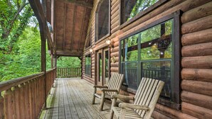 A wooden cabin with a porch, two rocking chairs, and large windows overlooking a forest.