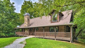 A log cabin with a stone chimney, a porch with railings, and a gravel path leading to the entrance.