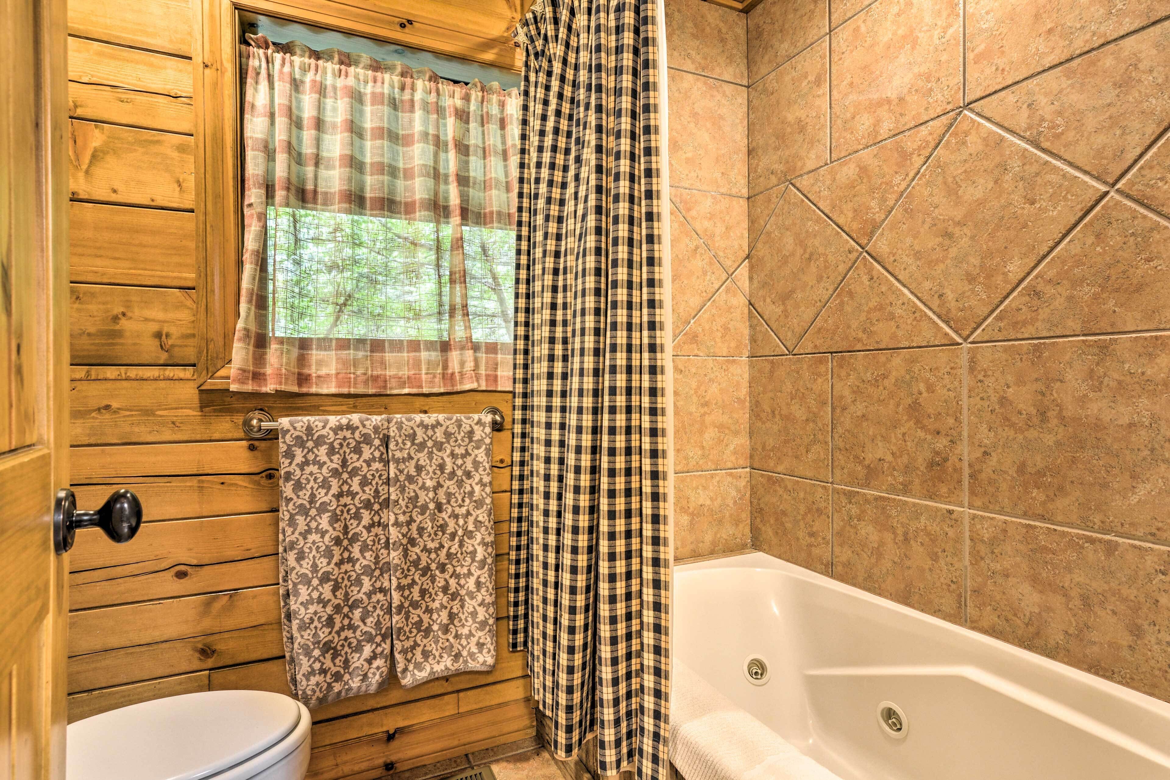 A bathroom with wooden walls, a window with a plaid curtain, a toilet, and a bathtub.